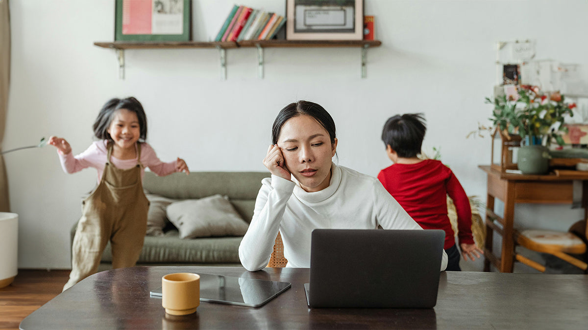 Mother on computer with children playing in background