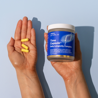 Two hands holding a jar of FutureLabs Time Capsule Daily Longevity Complex and yellow capsules against a light blue background.